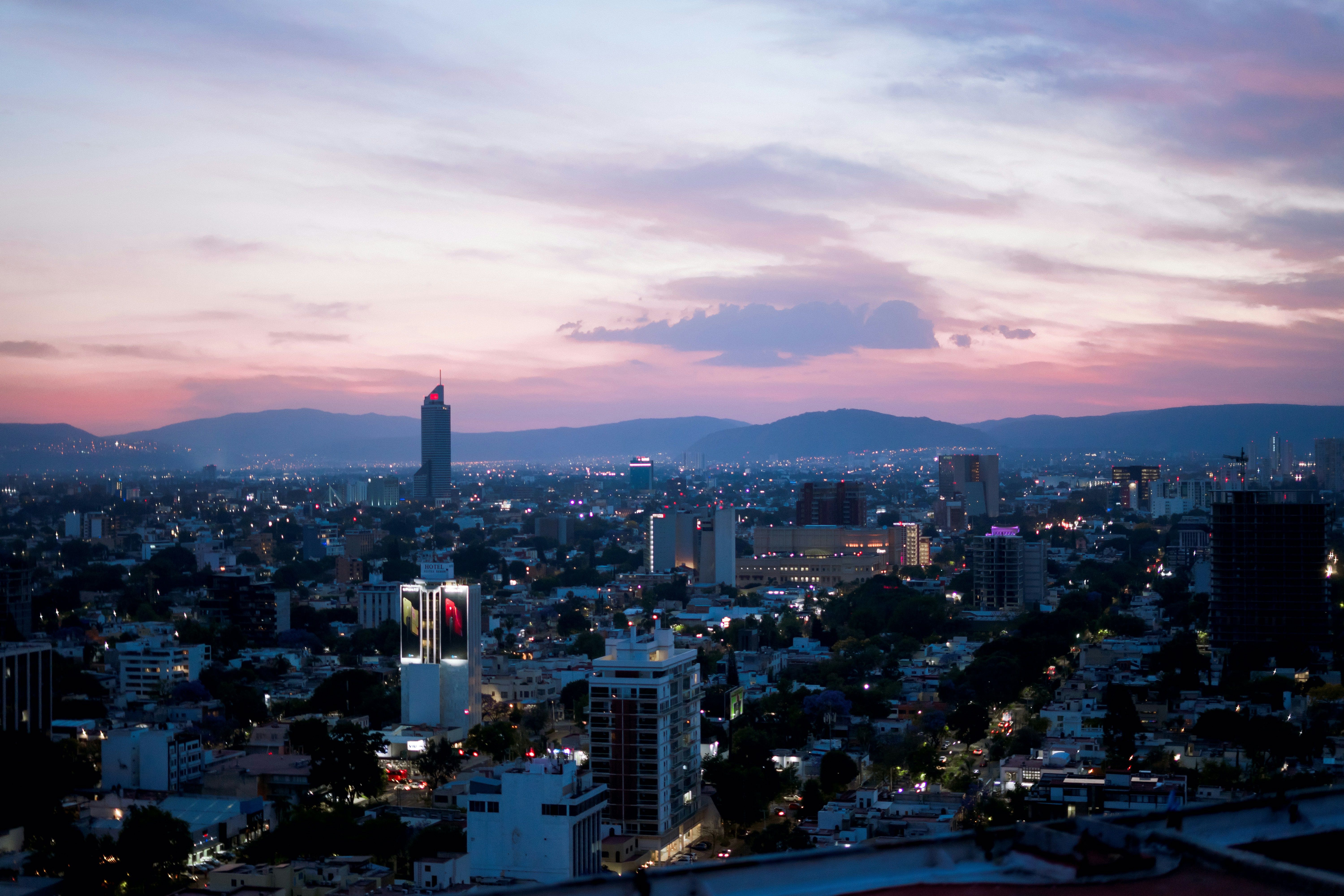 The Guadalajara skyline at dusk, with city lights and distant mountains under a violet sky